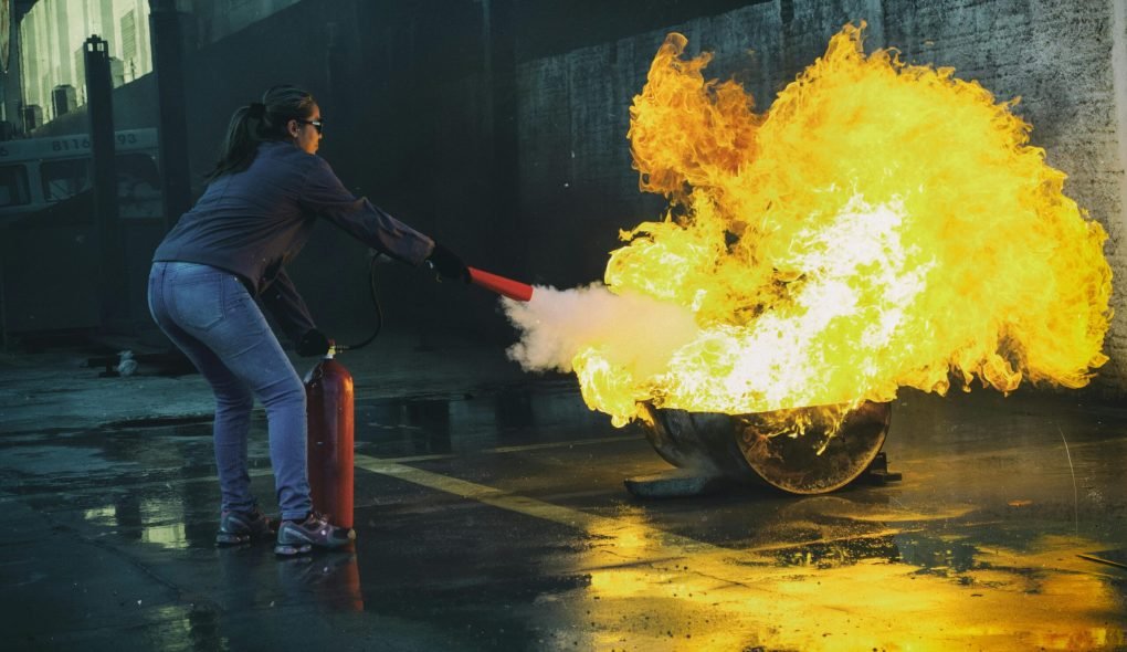 A woman uses a fire extinguisher to put out a large flame in an outdoor setting, showcasing fire safety.